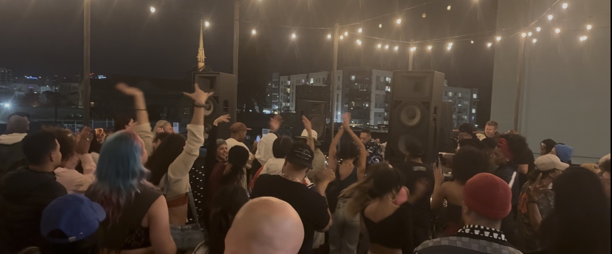 Crowd dancing on a rooftop under string lights at night
